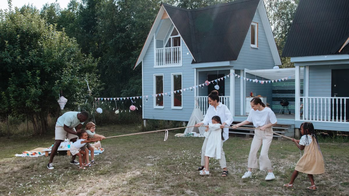 Happy family playing tug of war in front of cozy houses during a summer day.